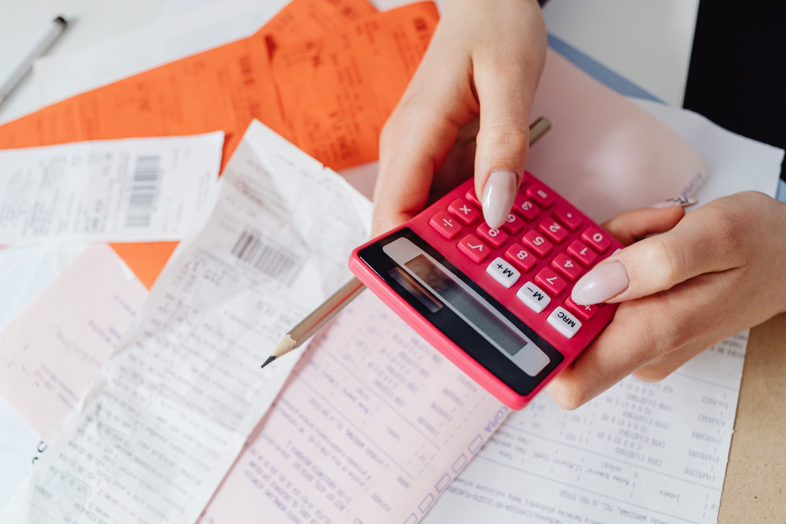 Mains utilisant une calculatrice rose parmi des factures